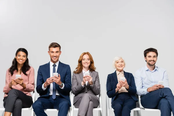 Smiling multicultural businesspeople using smartphones isolated on grey — Stock Photo