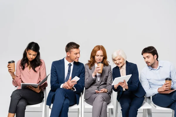 Senior businesswoman showing digital tablet near multiethnic businesspeople with coffee to go isolated on grey — Stock Photo