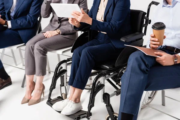 Cropped view of senior businesswoman in wheelchair holding digital tablet near colleagues on blurred grey background — Stock Photo