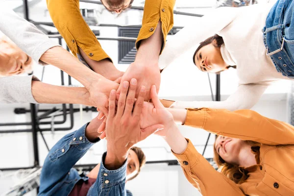 Vista inferior de personas multiculturales cogidas de la mano y sonriendo sobre un fondo borroso - foto de stock