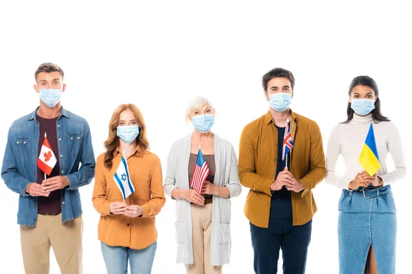 Multikulturelle Menschen in medizinischen Masken blicken in die Kamera, während sie Fahnen isoliert auf weiß halten — Stockfoto