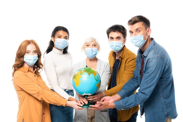 Multikulturelle Menschen in medizinischen Masken blicken in die Kamera, während sie den Globus isoliert auf weiß halten — Stockfoto