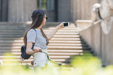 Smartphone cep telefonu ile sokakta selfie alarak güneş gözlüklü genç çekici kadın yan görünüm