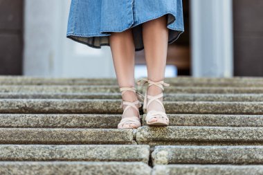 cropped shot of woman in denim skirt and fashionable shoes walking down steps clipart