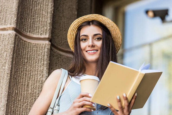 симпатичная улыбающаяся женщина с открытой книгой и кофе, чтобы выйти на улицу
