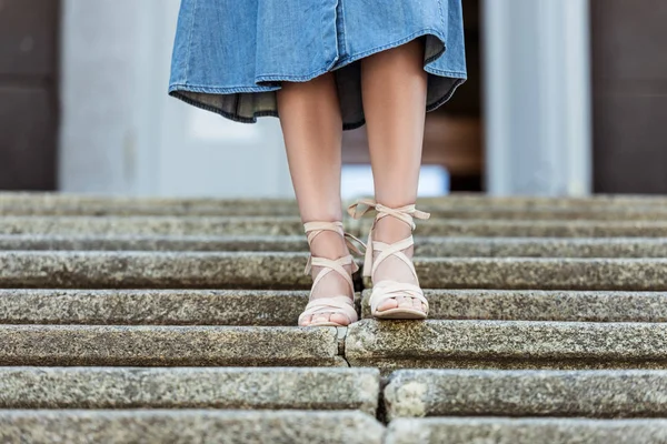 cropped shot of woman in denim skirt and fashionable shoes walking down steps