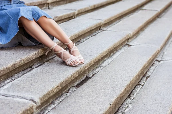 cropped shot of woman in denim skirt and fashionable shoes resting on steps on street