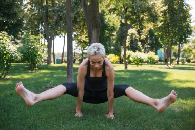Eller Yoga uygulamak ve üzerinde positing yapıyor sportif kadın parkta
