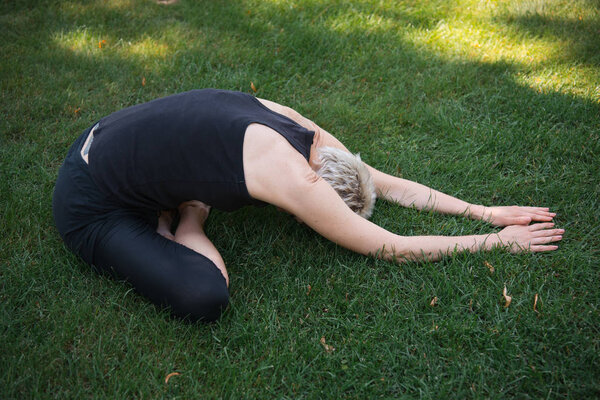 side view of woman practicing yoga in Wide Child pose (Balasana) on grass in park