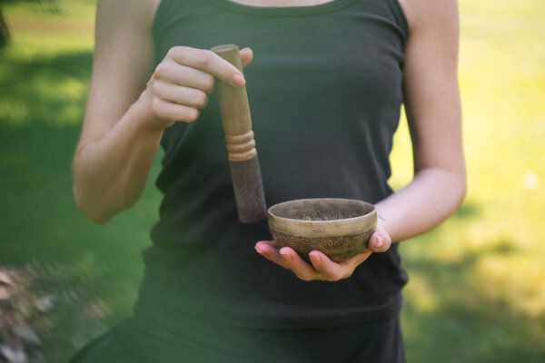 cropped image of woman making sound with tibetan singing bowl in park