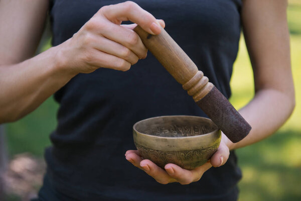 cropped image of woman making sound with tibetan singing bowl