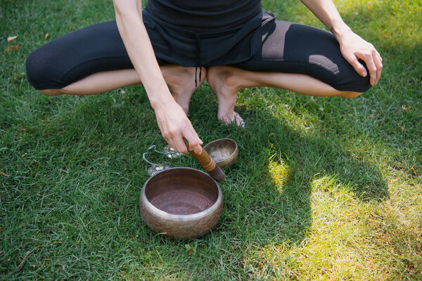 cropped image of woman squatting and making sound with tibetan singing bowls