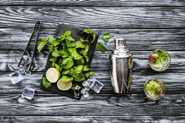 top view of fresh mint, tongs, shaker and strawberry kiwi mojito in glasses