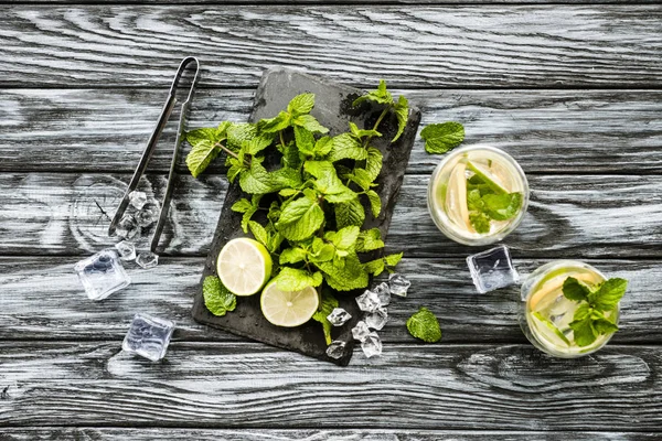 top view of mint, lime, ice cubes and glasses with mojito on wooden surface