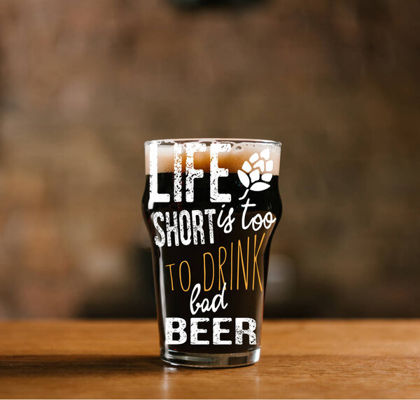 glass of fresh cold dark beer on wooden table in pub with "life is too short to drink cheap beer" inspiration
