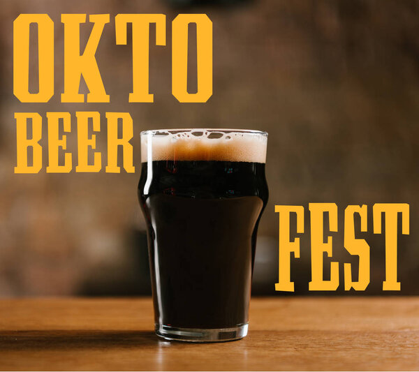 стакан холодного тёмного пива на деревянном столе в пабе с надписью "Октоберфест"
