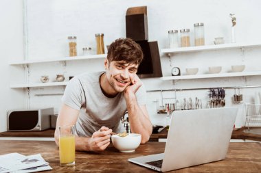 mutlu genç erkek freelancer kahvaltı ile laptop evde mutfakta masada Mısır gevreği yemek