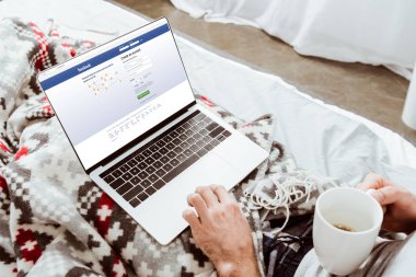 adam kahve fincanı holding ve evde yatakta ekranında facebook ile dizüstü bilgisayar kullanarak kırpılmış görüntü