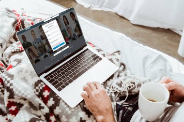 adam kahve fincanı holding ve evde yatakta ekranda LinkedIn ile dizüstü bilgisayar kullanarak kırpılmış görüntü