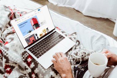 adam kahve fincanı holding ve ekran evde yatakta ebay ile dizüstü bilgisayar kullanarak kırpılmış görüntü