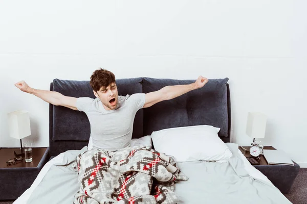 ハンサムな若い男あくびと朝時に自宅のベッドでストレッチ — ストック写真