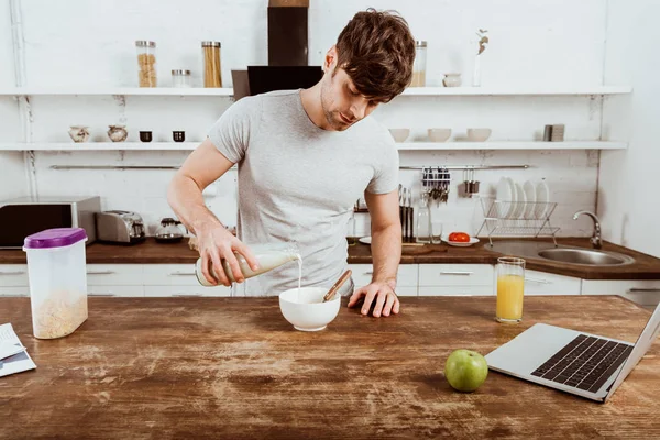 Male Freelancer Pouring Milk Bowl Corn Flakes Table Laptop Kitchen — Stock Photo, Image