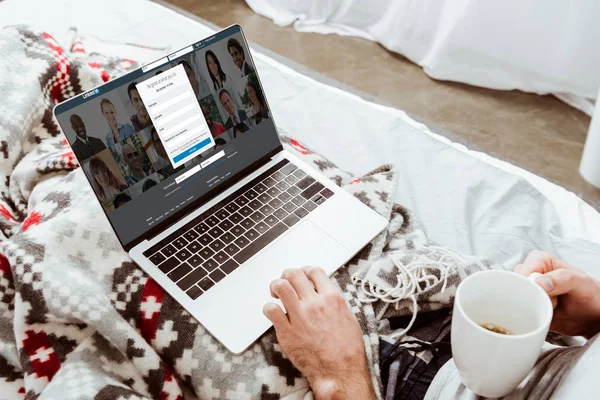 adam kahve fincanı holding ve evde yatakta ekranda LinkedIn ile dizüstü bilgisayar kullanarak kırpılmış görüntü