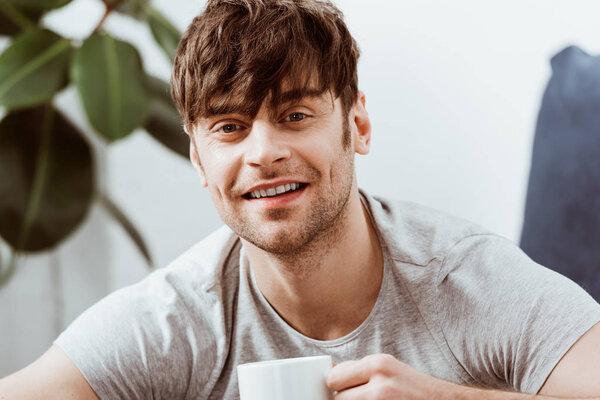 portrait of smiling man looking at camera and drinking coffee at home