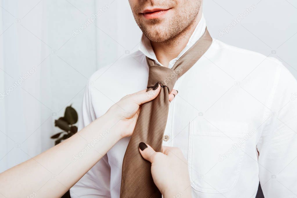 cropped image of woman tying neck tie to boyfriend in white shirt at home