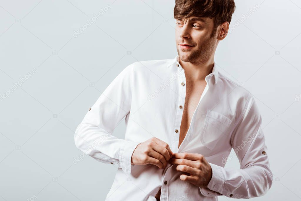 cheerful businessman buttoning up white shirt isolated on grey