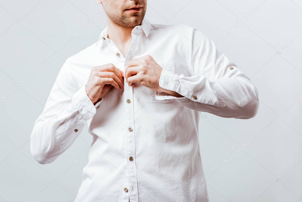 partial view of businessman buttoning up white shirt isolated on grey