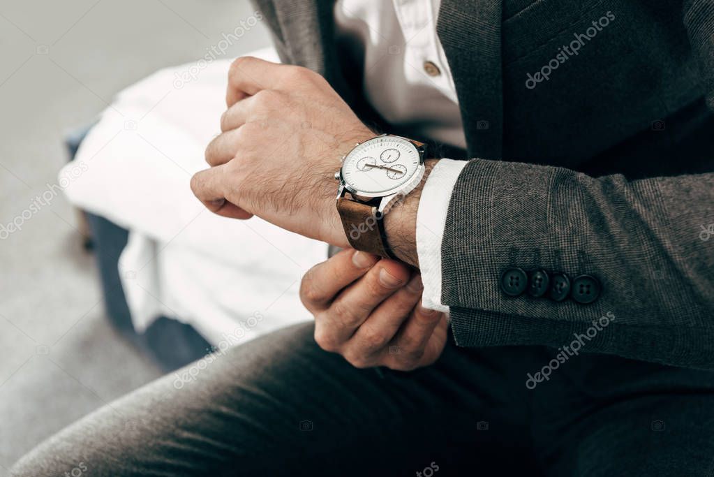 partial view of businessman in jacket putting on hand watch at home