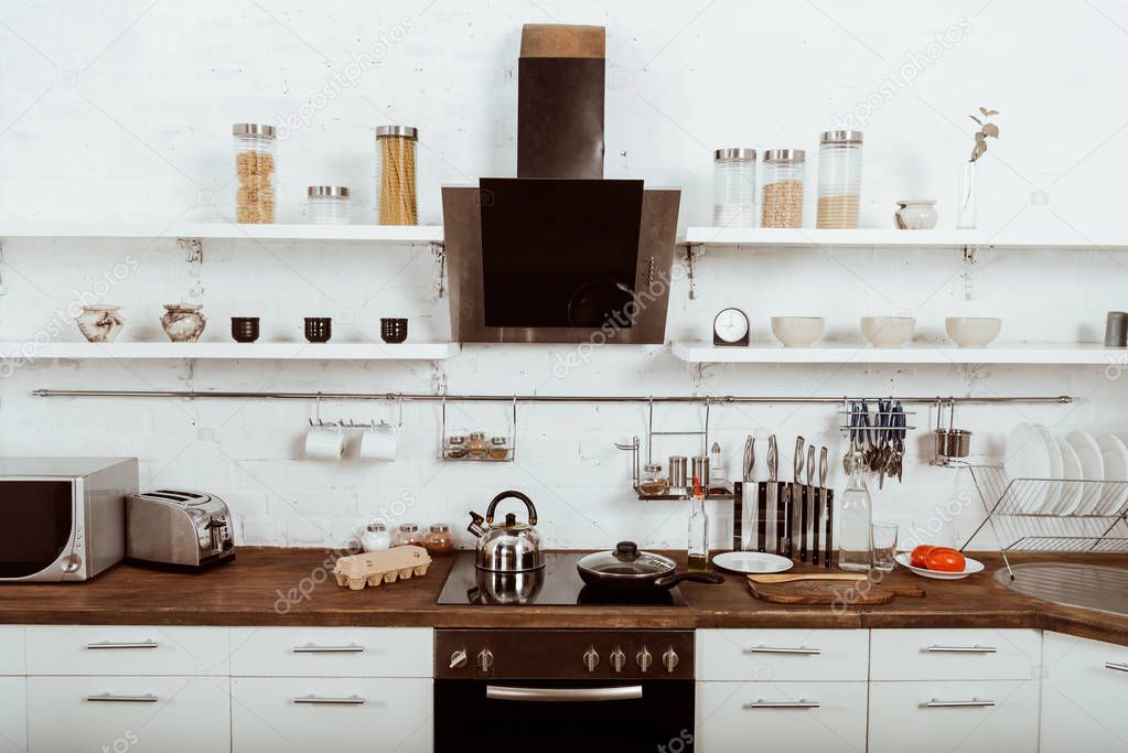 selective focus of modern kitchen interior with frying pan and teapot on stove 