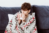 Selektiver Fokus eines Kranken, der zu Hause in eine Decke gehüllt Tee trinkt 