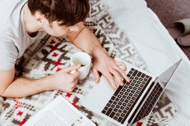 evde yatakta boş ekran ile dizüstü bilgisayar üzerinde çalışan kahve fincanı ile erkek Freelancer yüksek açılı görünüş