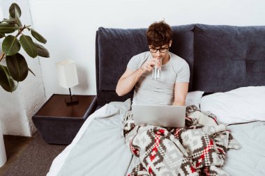 Erkek freelancer içme suyu ve çalışma üstünde laptop evde yatakta yüksek açılı görünüş