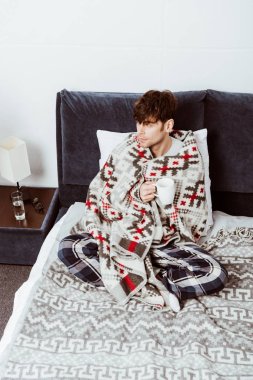 hasta adam yatakta evde çay ile oturup battaniyeye sarılmış yüksek açılı görünüş 