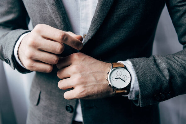 partial view of businessman with watch buttoning up jacket 