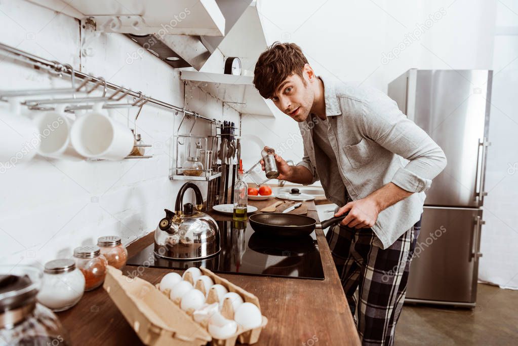 selective focus of young man cooking scrambled eggs on frying pan in kitchen 