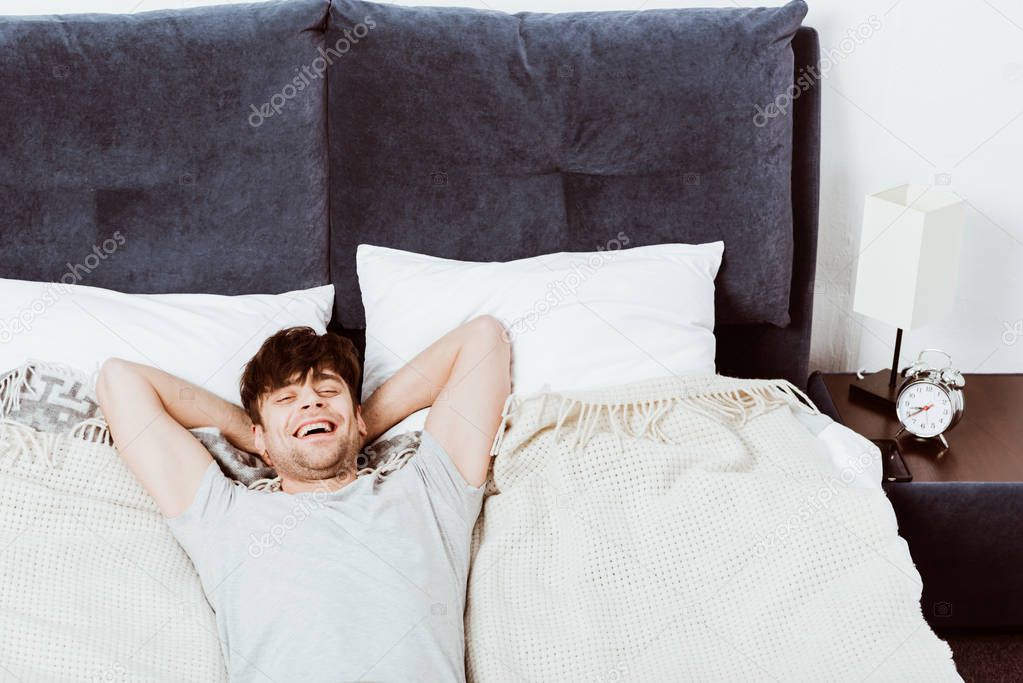 high angle view of laughing young man looking at camera and laying in bed at home