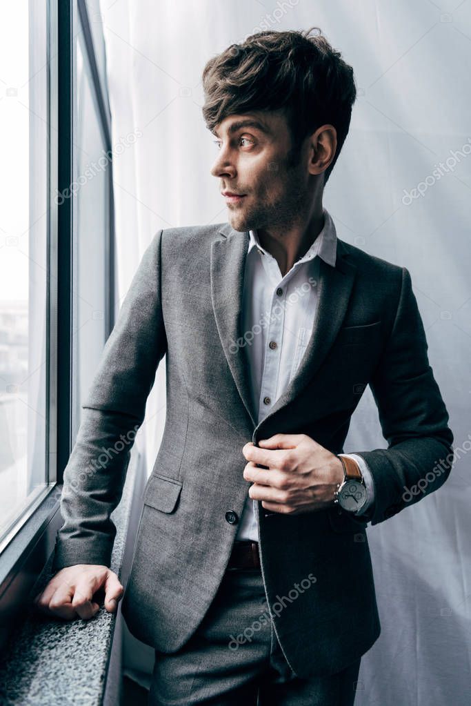 handsome businessman adjusting jacket and looking at window in office