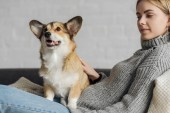 happy young woman relaxing on couch with her corgi dog