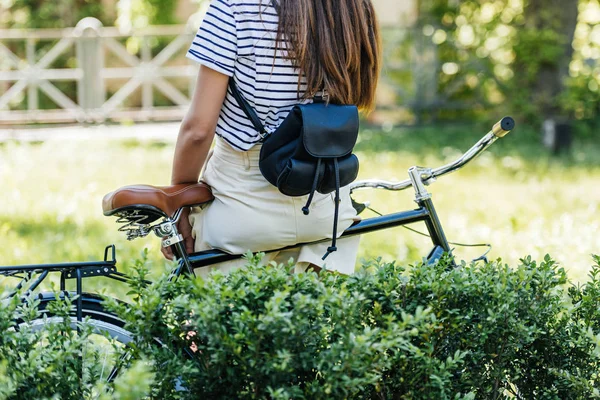 Cropped shot of woman with backpack sitting on retro bicycle in park — Stock Photo