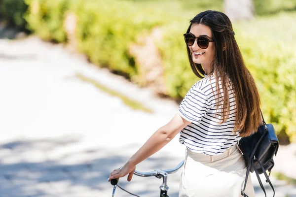Vista lateral de joven mujer sonriente en gafas de sol con bicicleta retro en la calle - foto de stock