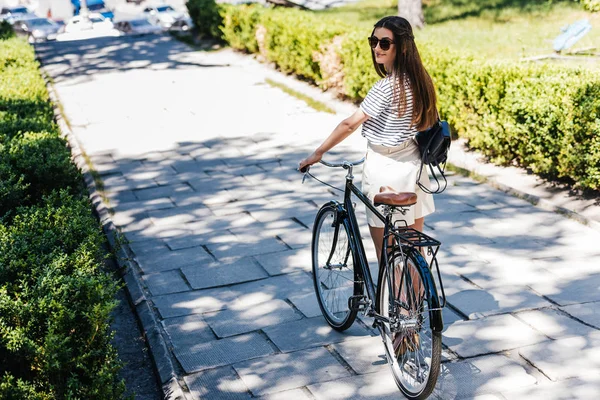 Вид ззаду молодої жінки в сонцезахисних окулярах з ретро-велосипедом на вулиці — стокове фото