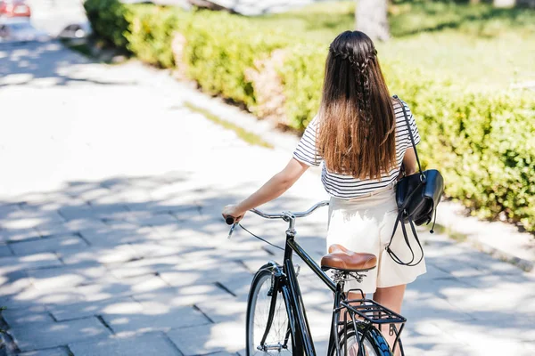 Visão traseira da mulher com bicicleta retro andando na rua — Fotografia de Stock