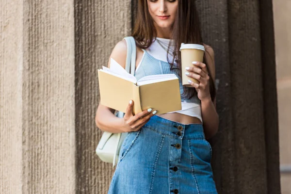 Vue partielle de jolie jeune femme lecture livre et café pour aller dans la rue — Photo de stock