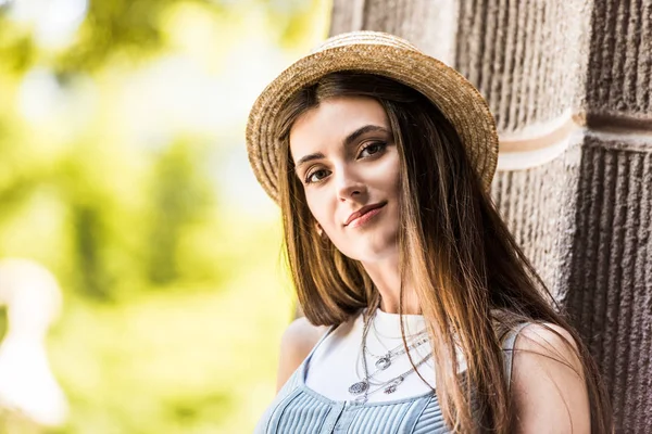 Retrato de hermosa mujer joven en sombrero de paja mirando a la cámara en la calle - foto de stock