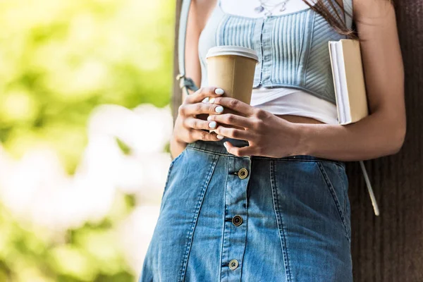 Частичный вид женщины с книгой и кофе, чтобы выйти на улицу — стоковое фото