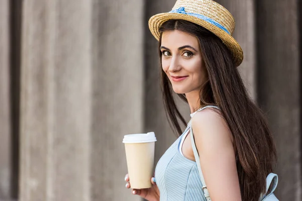 Vue latérale de jolie femme souriante en chapeau de paille avec café pour aller dans la rue — Photo de stock
